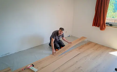 Handwerker verlegt Parkettboden in einem Raum, Fußbodenheizung & Parkett, Nahaufnahme des Bodens.