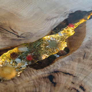 Holzplatte mit harzgefülltem Spalt, getrocknete Blumen und Gräser leuchten.