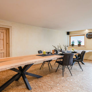 Esszimmer mit 7 Meter Holztisch und Stühlen, Kerze, Dekoration, helle Wände, Fenster und Tür.