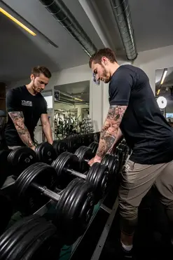 Trainer sortiert Kurzhanteln am Hantelregal im Fitnessstudio.