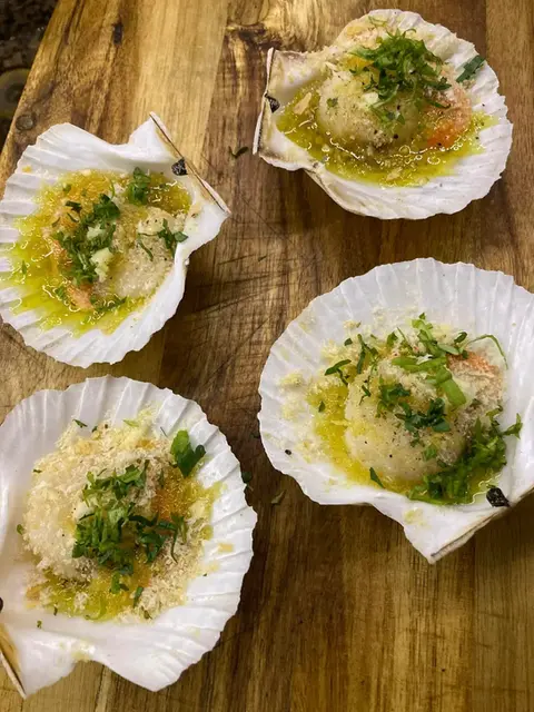 Jakobsmuscheln in Schale mit Kräutern und Butter auf Holzbrett.