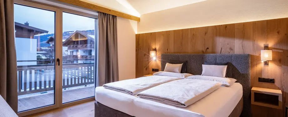Modernes Schlafzimmer mit Doppelbett, Holzverkleidung, indirekter Beleuchtung und Balkon mit Bergblick.