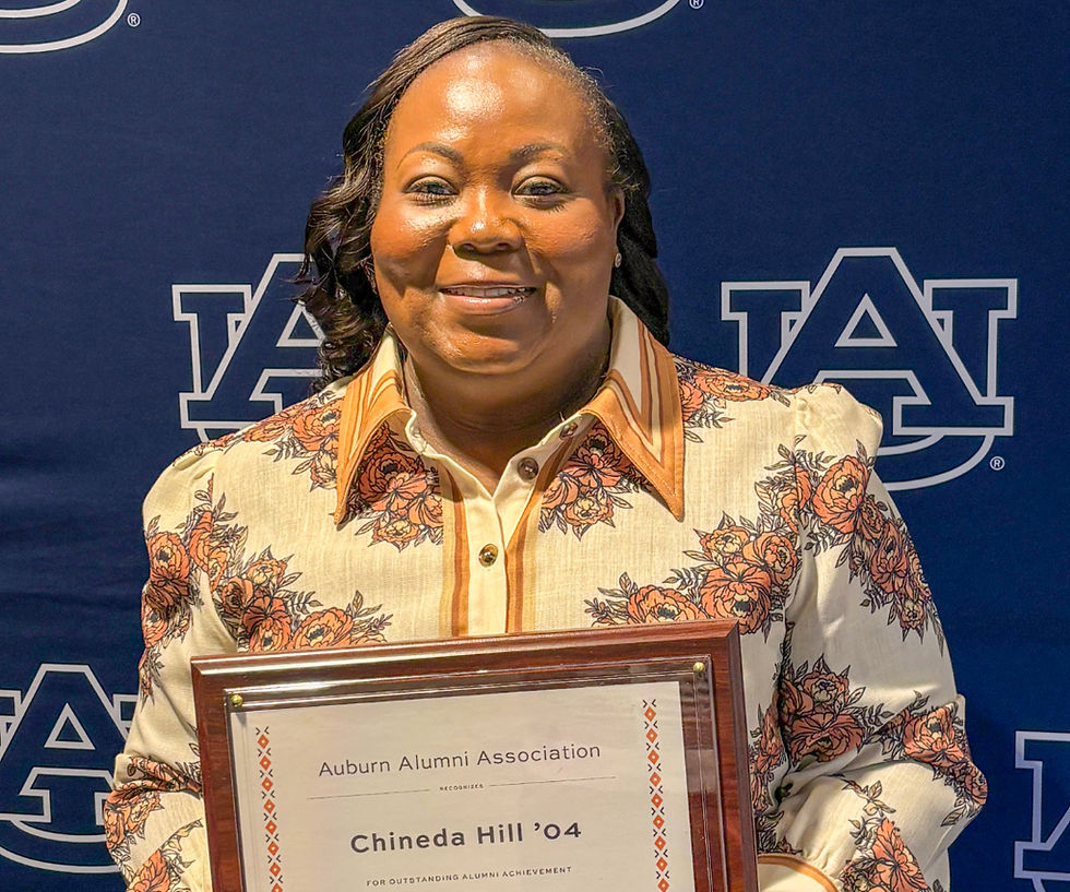 A woman in a cream colored dress with a floral pattern holds an award plaque.