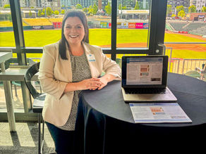 Graduate student Abby Bell stands at a table with a laptop and handouts.