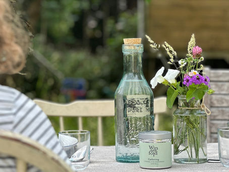 Outdoor dining in a country garden with a citronella candle, rustic water jug and posy of flowers on the tablecloth.