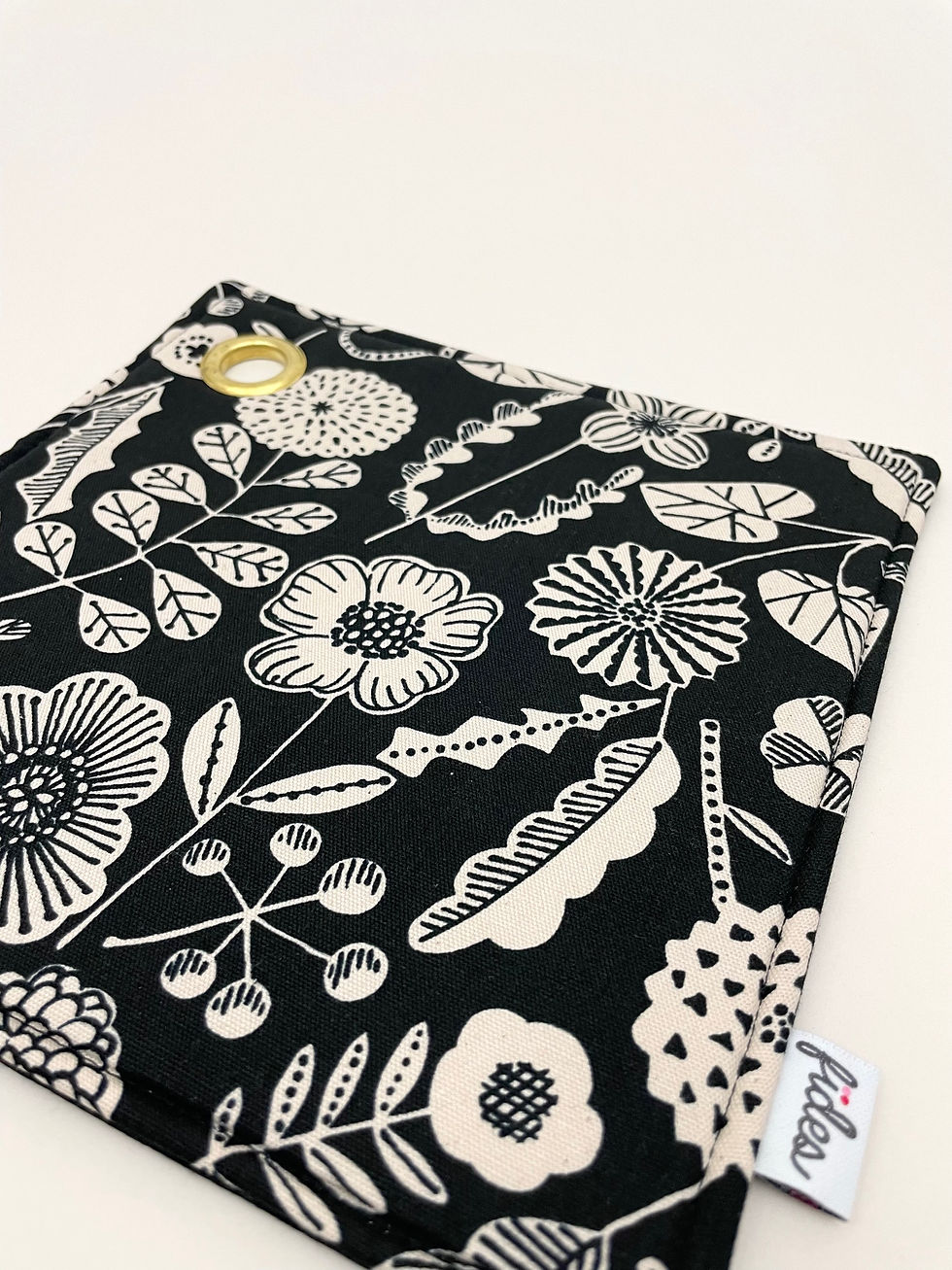 Miniaturbild: Schwarzer Topflappen mit hellen Blumen und Messingöse