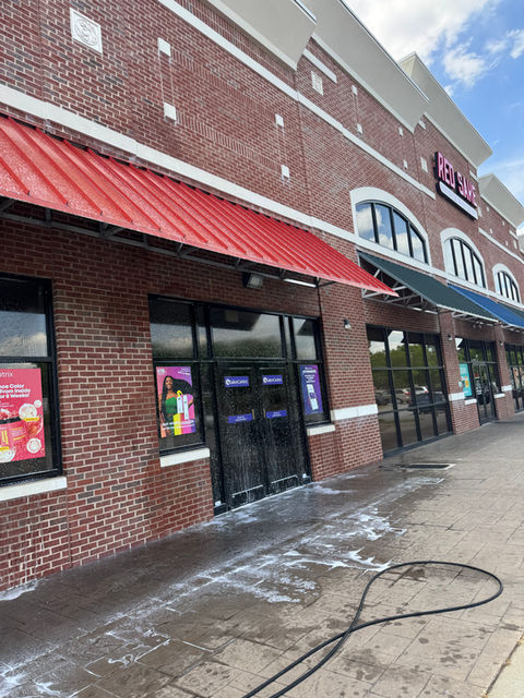 Brick storefront with red awning, wet from pressure washing