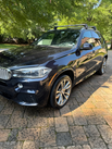 Dark blue BMW SUV parked on a paved driveway with roof rack