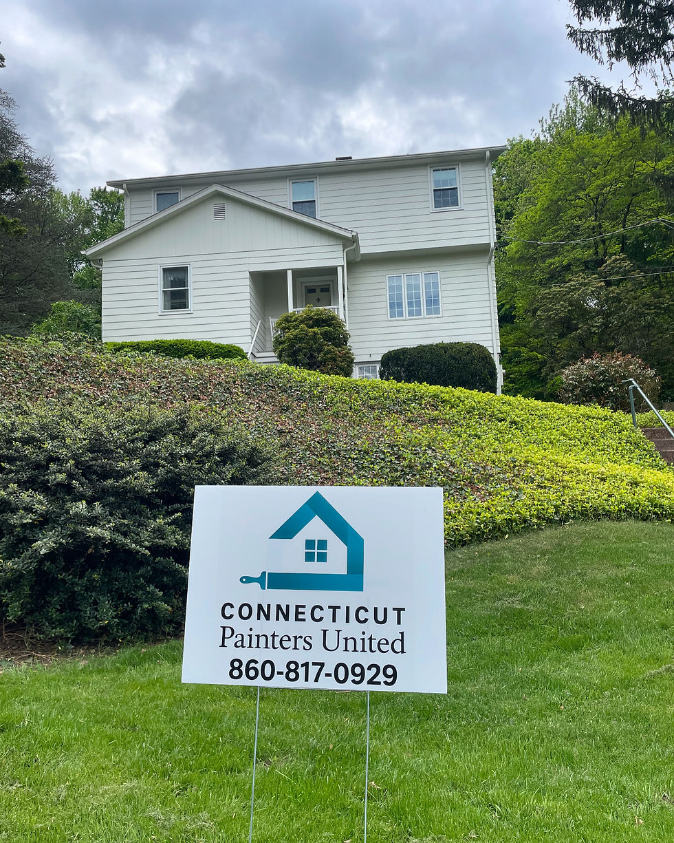 White two-story house with lush greenery in front. A sign on the lawn reads "CONNECTICUT Painters United 860-817-0929" under cloudy skies.