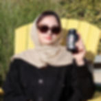 Woman in hijab holding Alnima Collagen Peptides Complex bottle while sitting on yellow chair outdoors, promoting beauty and w