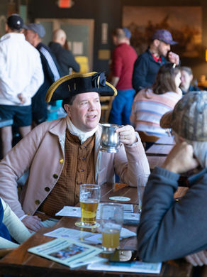 Historic reenactor dressed in late 18th century garb chats with 21st century patrons in a tavern