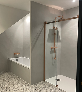 Salle de bain sur mesure au style contemporain, avec douche à l’italienne vitrée, baignoire intégrée, robinetterie finition cuivre et sol terrazzo. L’ensemble crée une ambiance élégante, minimaliste et haut de gamme, pensée pour allier confort, sobriété et qualité des finitions.