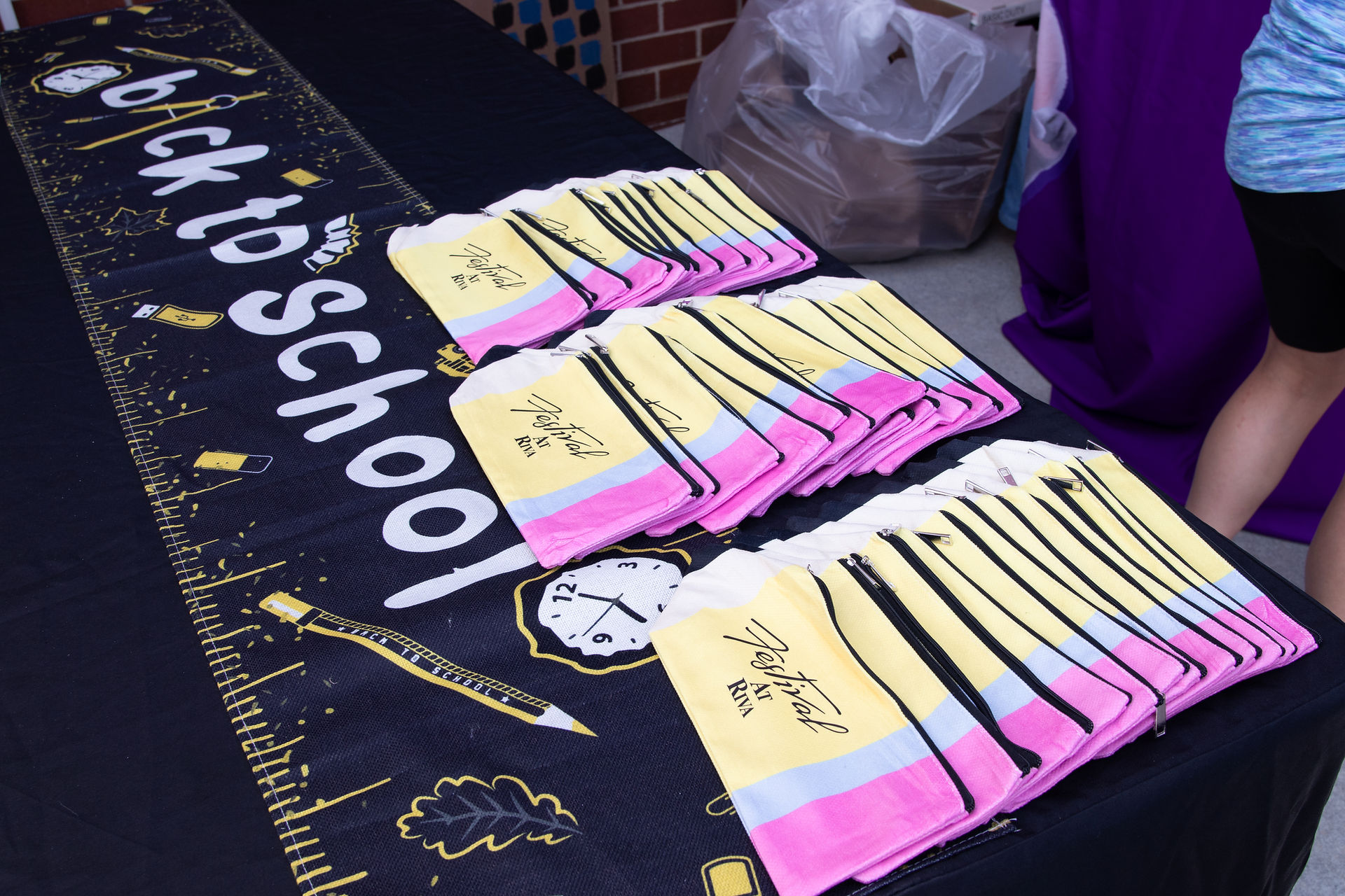 Image showing a table filled with vibrant, branded pencil pouches, ready to be handed out to event guests, with eager children and parents lining up in the background.