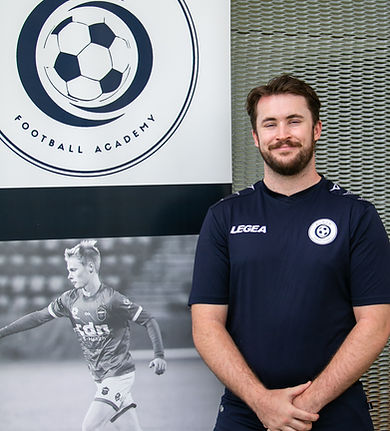 Lead Coach Harry Byrnes standing next to ELEV8 Football Academy banner located at Bowral Football Club