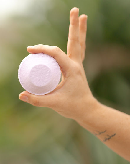 Close-up of The Radiant Rhino lavender shower steamer held outdoors against natural green background