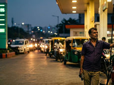 Man refueling at petrol station with traffic queue showing rising fuel demand pressure in India