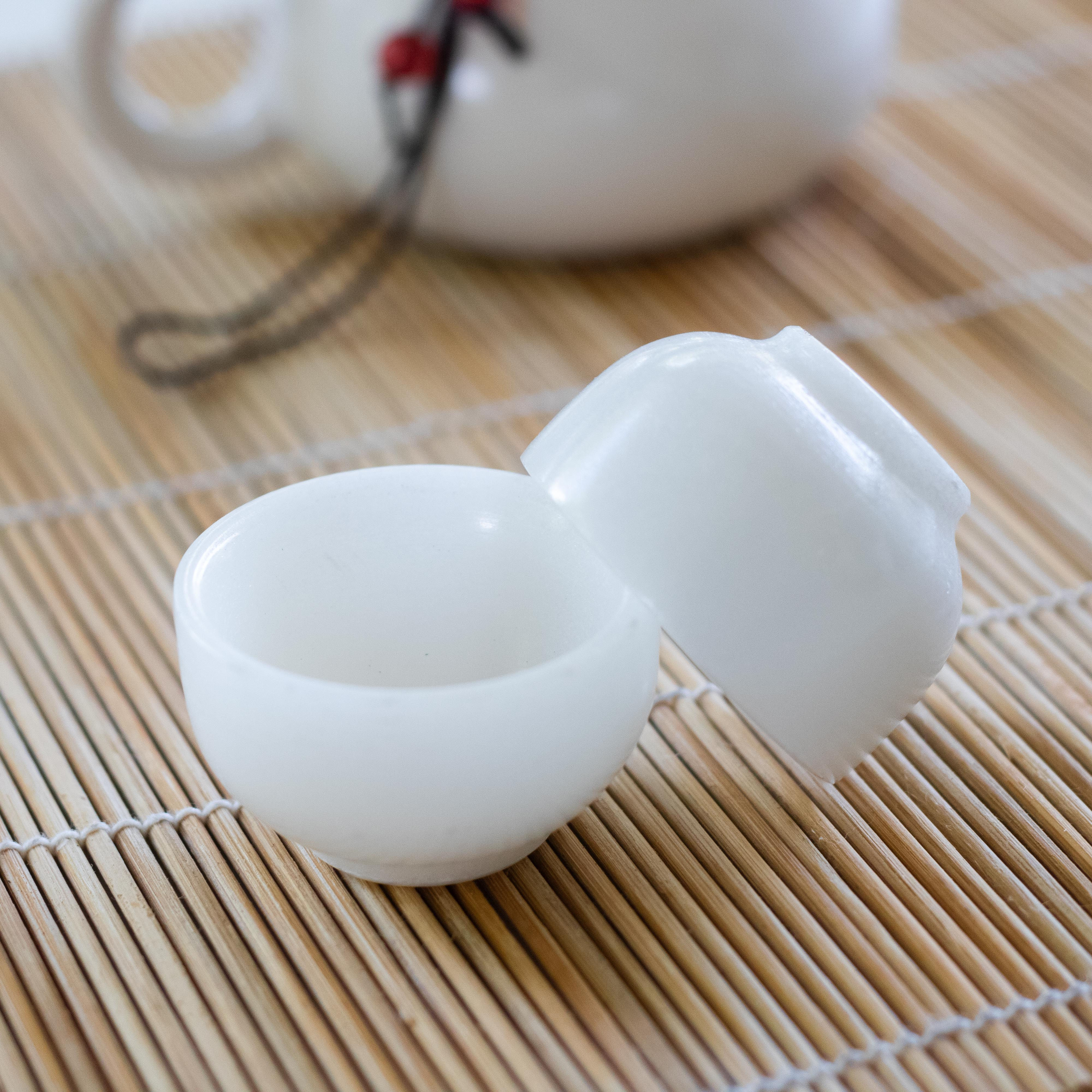Two petite white jade porcelain tea cups on a bamboo mat beside a teapot—minimalist elegance in every sip.
