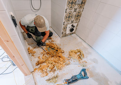 A worker removes rotted subfloor and insulation from a bathroom using a crowbar Visible si