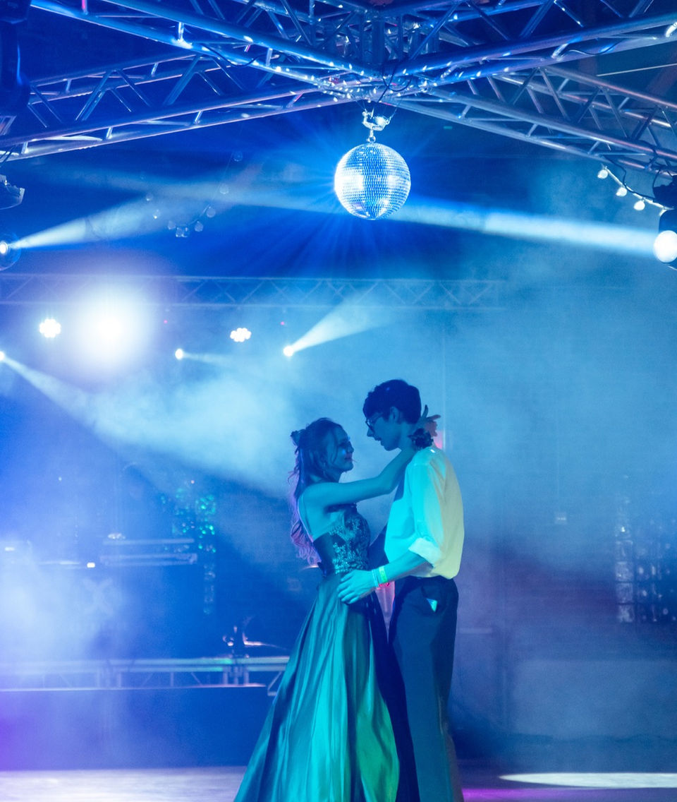 boy and girl at high school prom under mirror ball and lights 