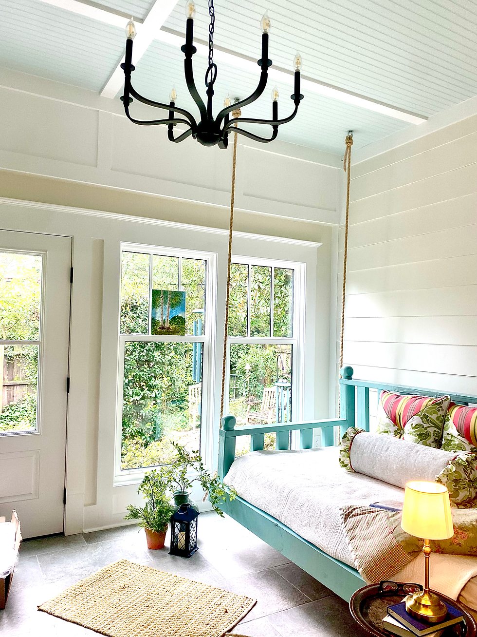 Bright sunroom in a 1920s Wilmington Craftsman home with swing-style daybed, airy blue ceiling, and black chandelier.