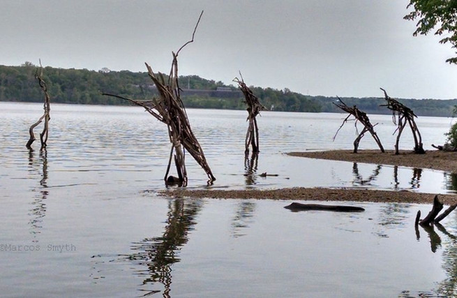 Abstract wood figures suggesting boat refugees reaching land.