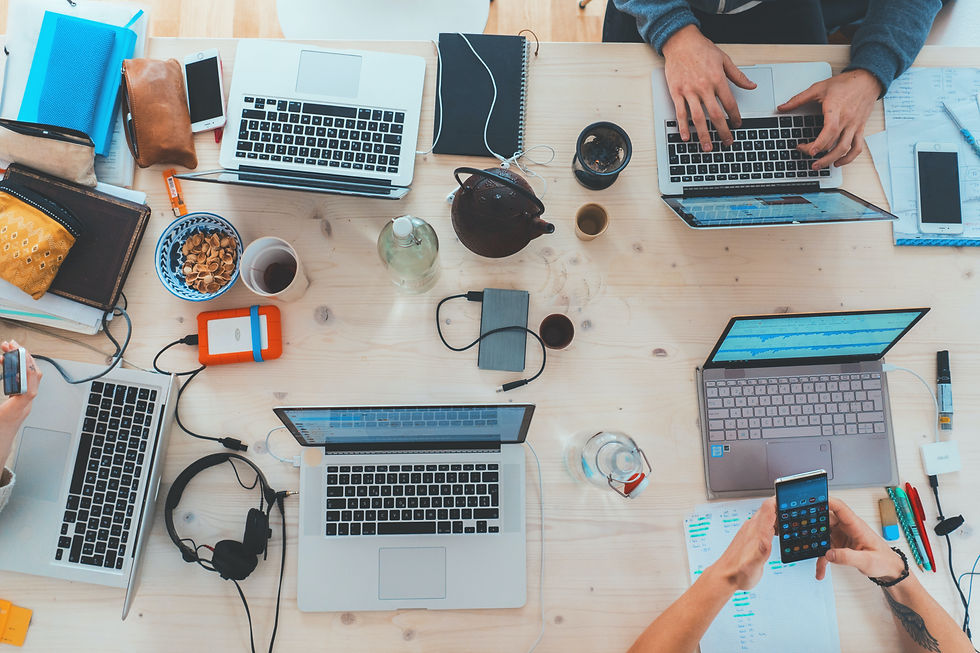 Several books, laptops, phones, and other digital devices are all crowded on a single work table as a representation of information overload.