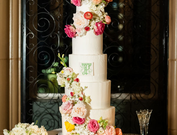Classic white wedding cake with vibrant pink, orange, and yellow floral decorations