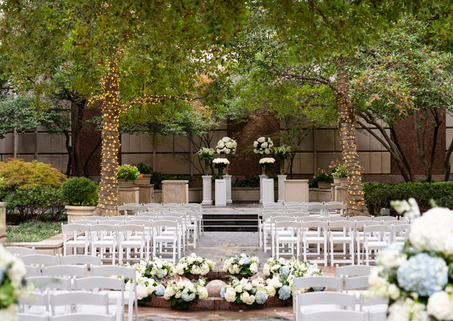 Outdoor wedding ceremony at Hotel Crescent Court featuring white chairs, floral arrangements, and garden greenery