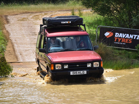 Red Landrover Discovery driving through water.