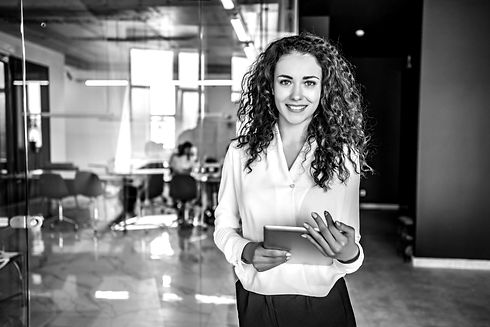 The image depicts a cheerful female employee holding a tablet device. She has a positive expression on her face, suggesting happiness and contentment. Her body language indicates a sense of belonging and connection to the organization. The tablet she is holding may represent technology or digital tools used in the workplace. Overall, the image conveys a positive and engaged employee who feels a strong sense of affiliation with the organization.