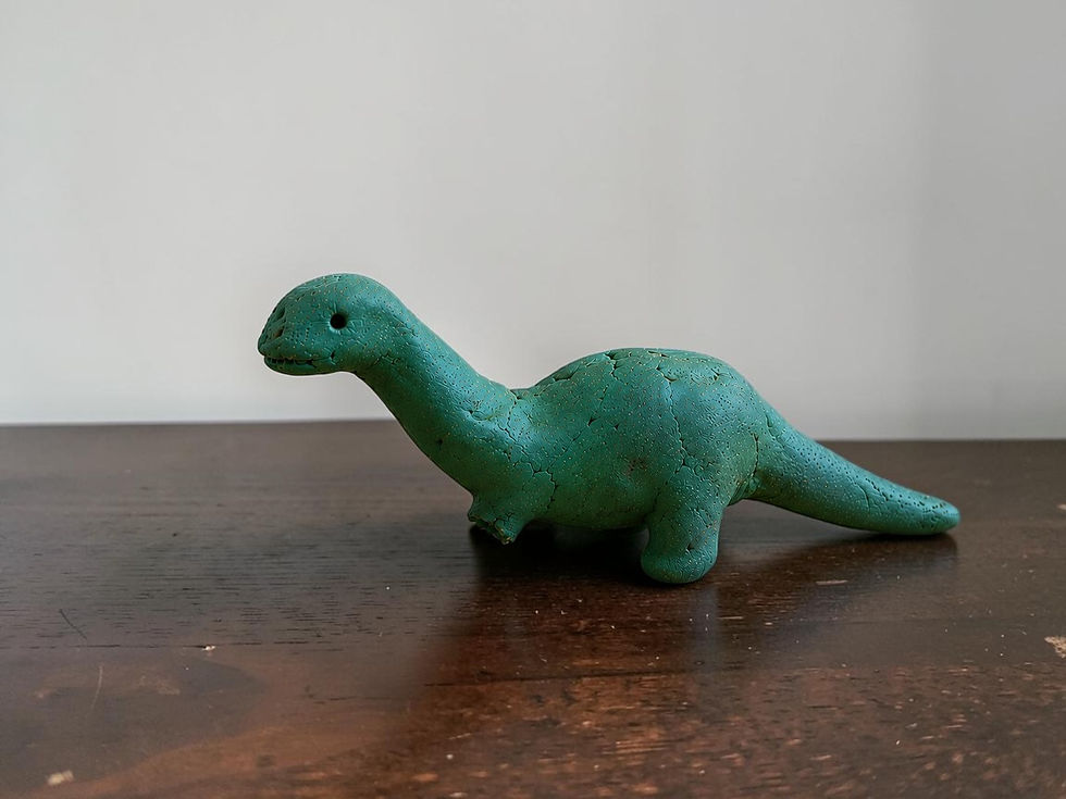 A green clay dino with a broken leg on a brown wooden table