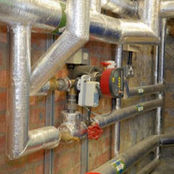 Silver foil wrapped heating pipework and valves in commercial plant room