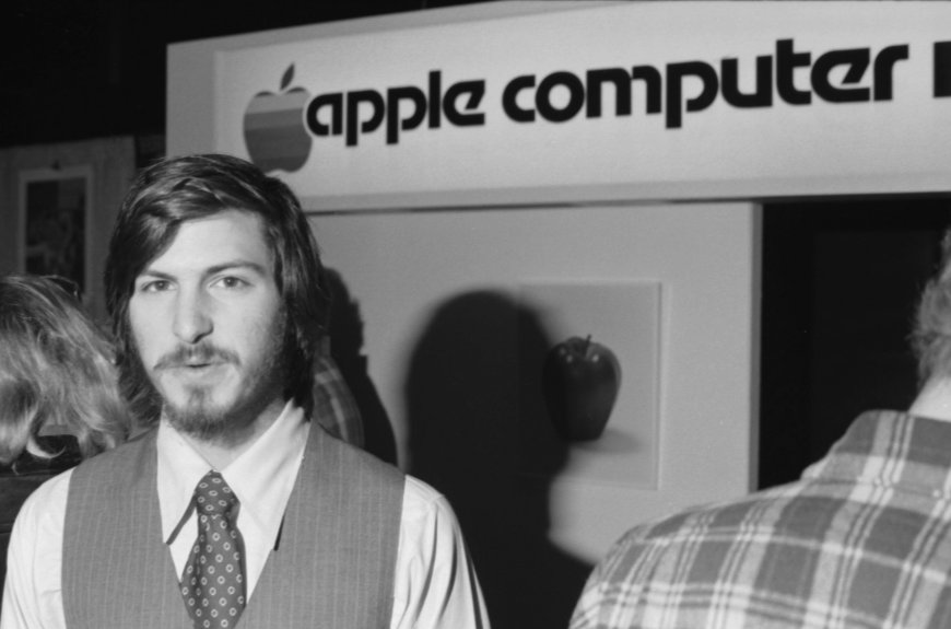 Archival photograph of Steve Jobs beside early Apple Computer signage