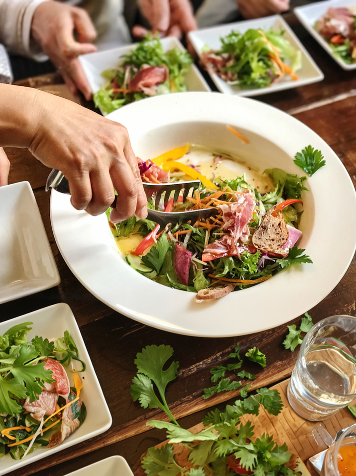Person serving fresh green salad with tongs into individual plates.