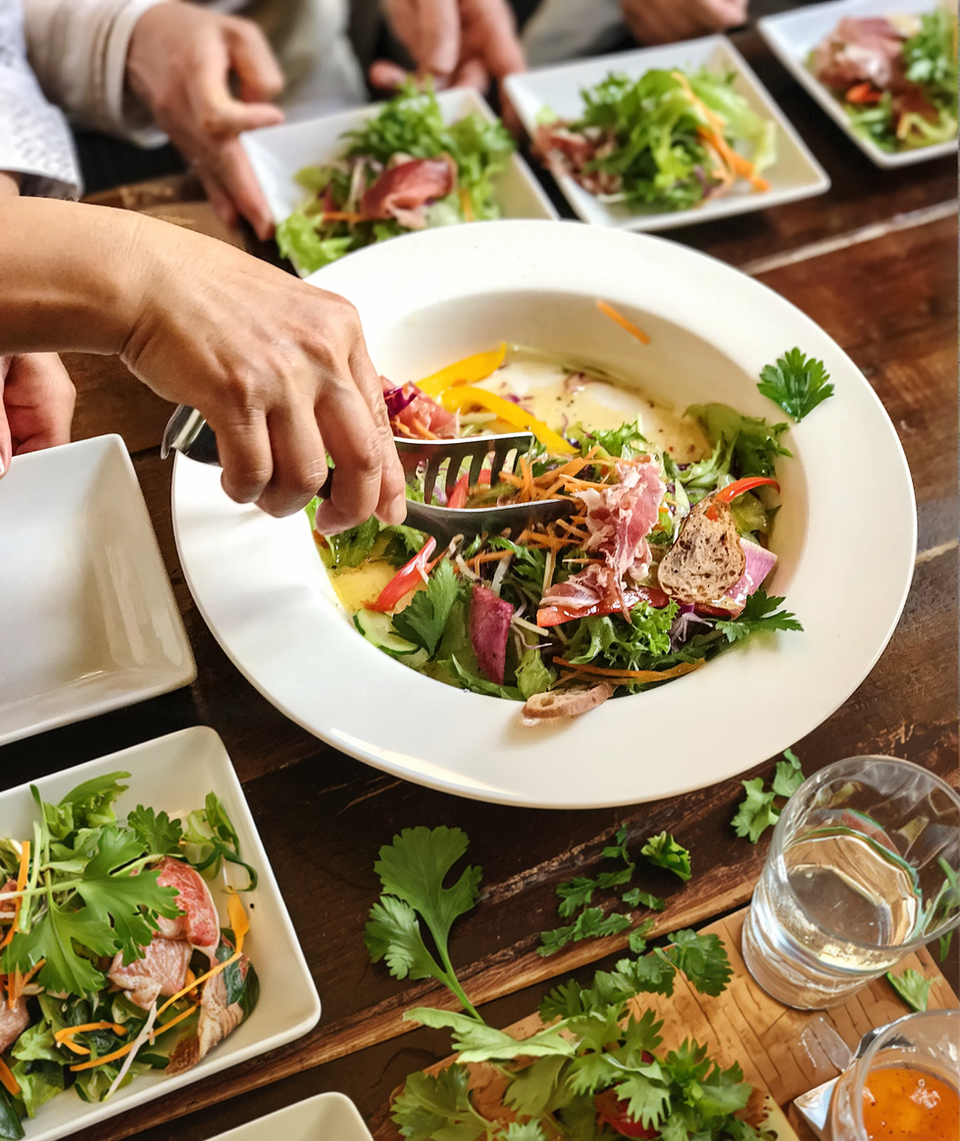 Person serving fresh green salad with tongs into individual plates.