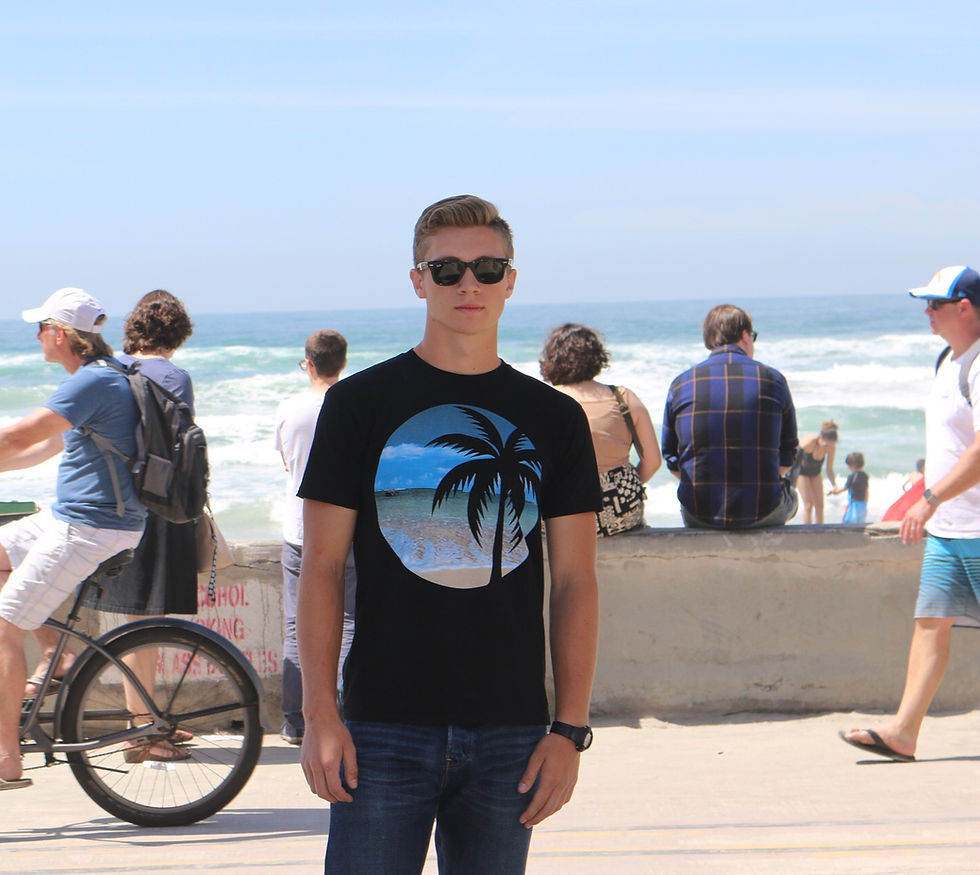 Young man in black shirt with palm tree graphic stands at beach