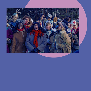 A group of singers stands outdoors with trees in the background, some holding props. Vibrant attire and lively expressions create a festive mood.