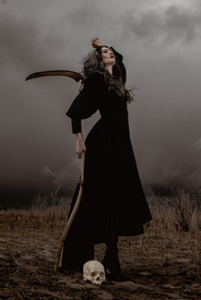 Incredible scene of gothic woman holding scythe above skull beneath a storm dressed in all black