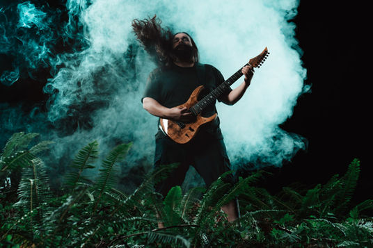 Metal enthusiast plays guitar in the dark and smoky pacific northwest woods