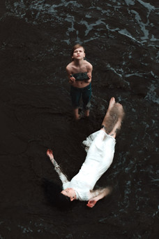 Surreal scene of boy holding stone finding cast away woman in tide