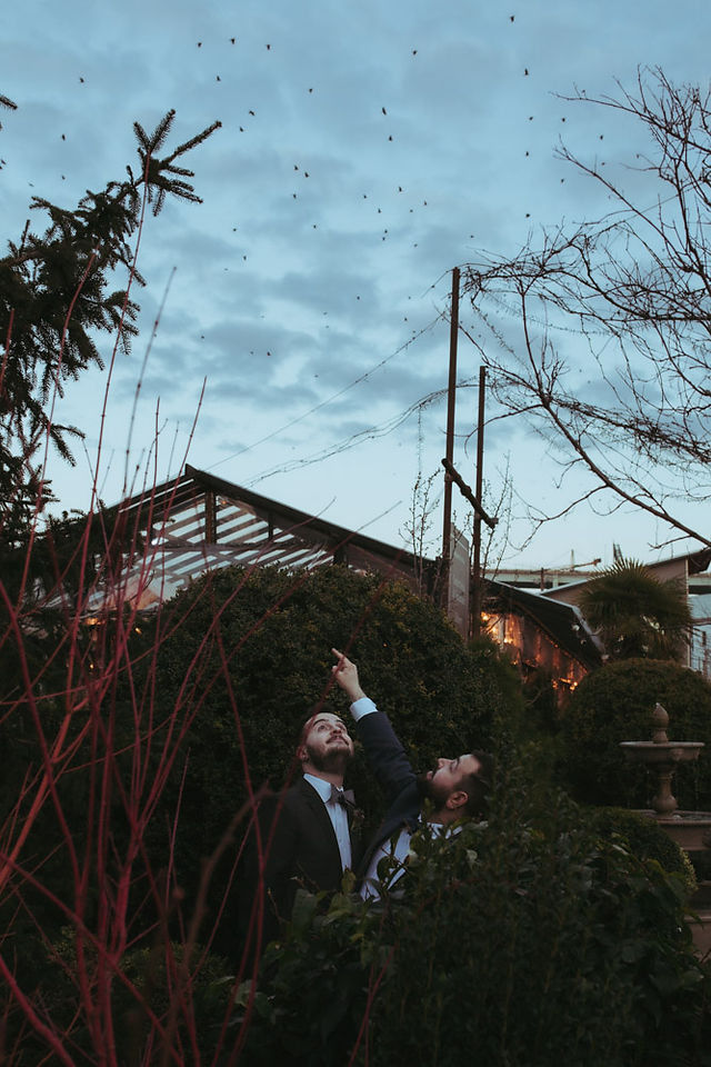 Grooms snuggle and pose for wedding photographer in front of nursery wedding venue