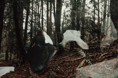 Surreal scene of gothic person in black dress running through faded white sheets in forest