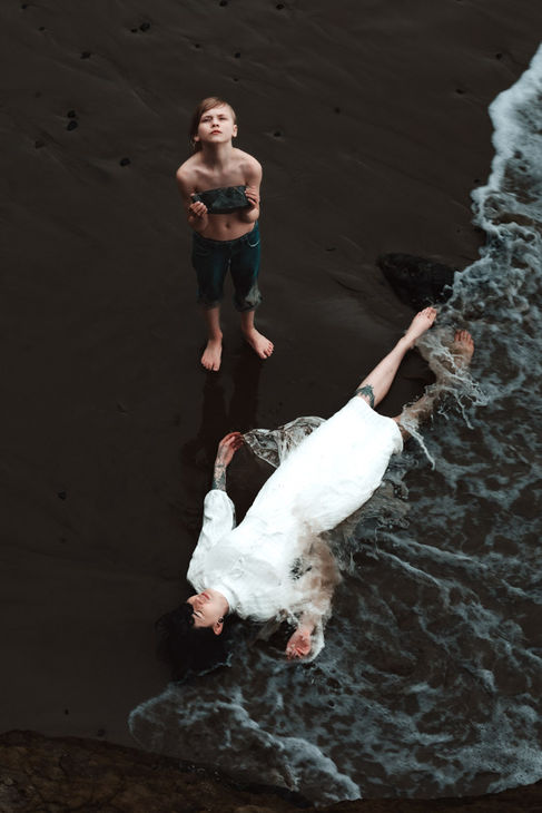 Fine art portrait of woman laying in waves and boy holding a rock