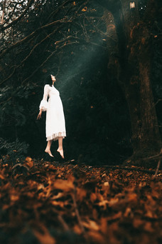 Surreal scene of a woman in white floating in forest above fall leaves