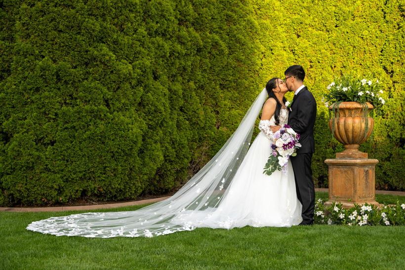 Traditional bride and groom kiss in front of giant hedge wall