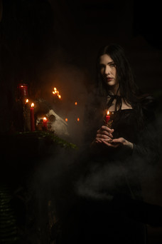 Gothic portrait of woman in black in the dark with red candles and skull on a fireplace mantle