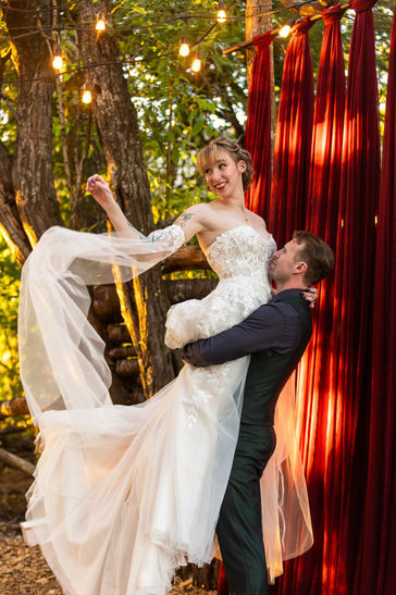 Sun kissed bride and groom in green in front of shaded red curtains in Oregon forest