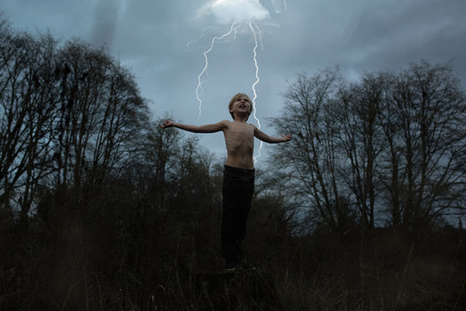 Young boy raises arms to the sky as lightning strikes