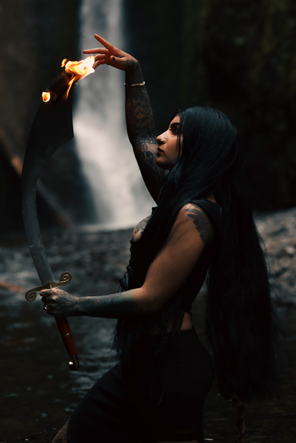 Golnar wielding a flaming sword in front of a majestic waterfall