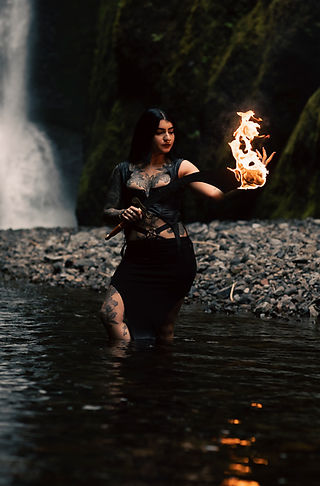 Golnar wielding a flaming sword in front of a majestic waterfall